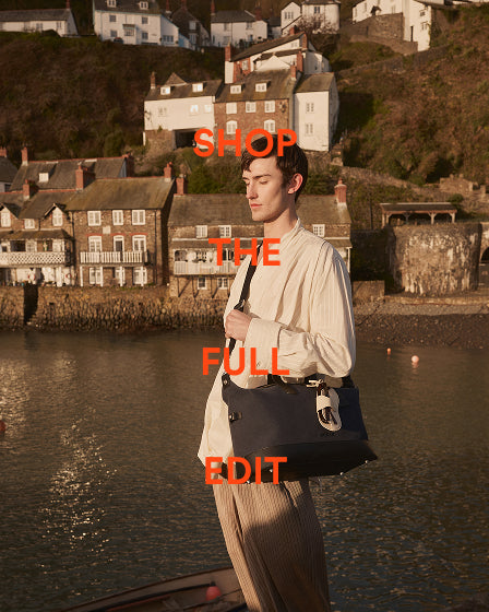 a man standing on a dock with a bag in front of a body of water